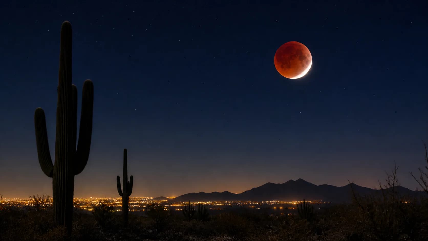 Copper-red partial lunar eclipse above Arizona desert with saguaro cactus silhouettes.